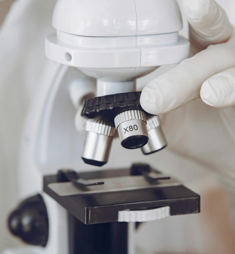 Gloved scientist adjusting a microscope in a laboratory setting, focusing on optics and research.